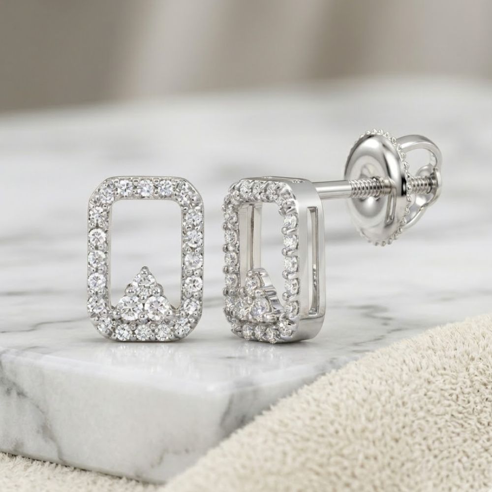 A pair of 1/6CTW natural diamond earrings in 10K gold with a rectangular shape, rounded corners, and an arrow-like accent, shown on marble with a beige cloth nearby.