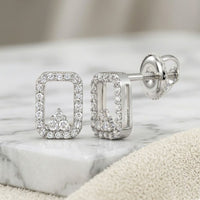 A pair of 1/6CTW natural diamond earrings in 10K gold with a rectangular shape, rounded corners, and an arrow-like accent, shown on marble with a beige cloth nearby.