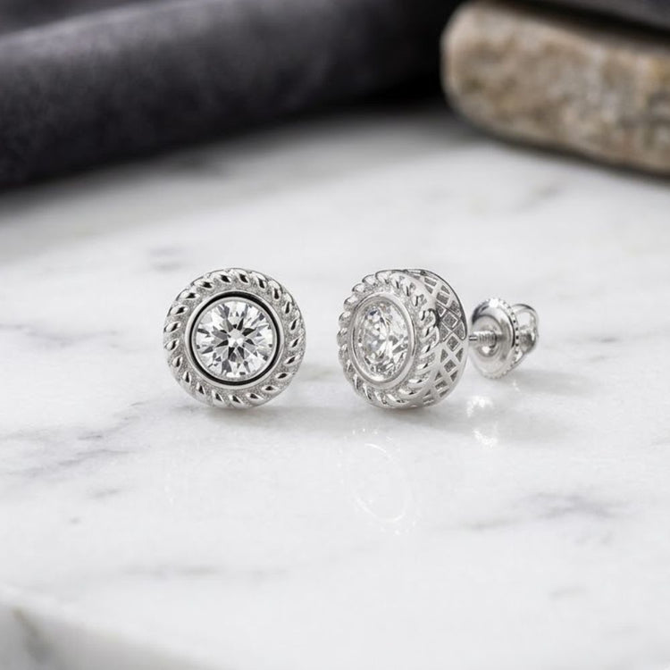A pair of 1/2CTW Diamond Solitaire Men’s Earrings crafted in 10K gold, featuring round, silver-toned studs with braided edges and sparkling clear diamonds at the center, reminiscent of a classic men’s solitaire earring style, elegantly displayed on a white marble surface.