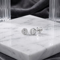 10k Gold Round Diamond Stud Earrings 1/6 Cttw, featuring intricate diamond detailing and set in 10k gold, are displayed on a white marble slab with clear glass and dark velvet in the background.