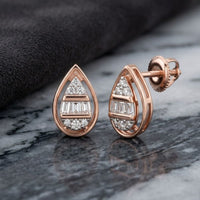 A pair of 1/10 CTW Natural Diamond Pear Earrings in 10k Gold, shown on a marble surface beside a folded dark cloth.