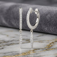 A pair of 10k White Gold Diamond Drop Dangle Earrings featuring diamond-adorned marquise-shaped pendants, showcased on a marble surface against a gray fabric backdrop.
