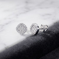A pair of 1/6CTW Clover Diamond Earrings in 10k gold, featuring secure screw-back posts and elegantly displayed on a marble surface beside black textured fabric, exude timeless elegance—perfect for those who appreciate the refined allure of fine gold jewelry.
