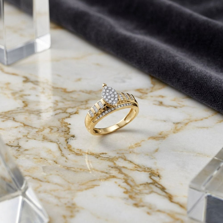 The 10k Gold Oval Diamond Cluster Bridal Ring 1/2 Cttw rests elegantly on a marble surface, its sparkling cluster of oval-shaped diamonds beautifully complemented by additional diamonds set along the band. Acrylic blocks and dark gray fabric provide an elegant backdrop, highlighting this exquisite bridal engagement ring.
