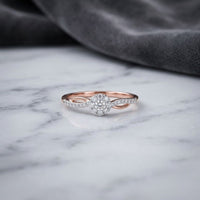 A 10k Yellow Gold Round Diamond Halo Promise Ring (1/5 Cttw) rests on a white marble surface, with a folded gray fabric in the background.