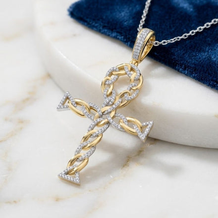 The 10K Gold Diamond Ankh Cross Pendant 3/8 CTW, crafted from yellow gold with braided details and sparkling diamonds, rests on a marble surface beside a blue velvet cloth.