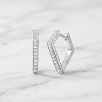 Two geometric, V-shaped huggie hoop earrings crafted in 10k gold and set with a total of 1/3 CTW natural diamonds are displayed on a white marble surface.