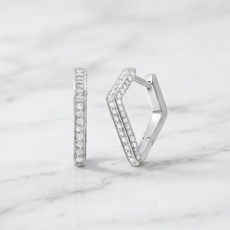 Two geometric, V-shaped huggie hoop earrings crafted in 10k gold and set with a total of 1/3 CTW natural diamonds are displayed on a white marble surface.