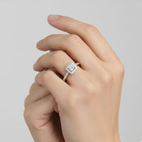 A hand with neatly manicured nails showcases the 10k Gold Princess Diamond Halo Engagement Ring on the ring finger, set against a plain light gray background.