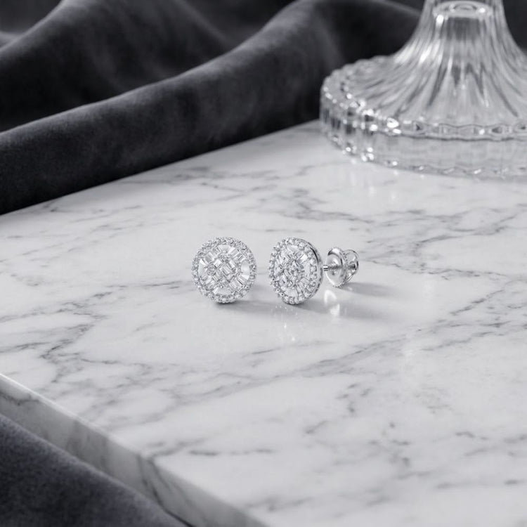 A pair of 10K Gold Baguette Diamond Circle Earrings 5/8 CTW are displayed on a white marble surface, with a glass lid and dark velvet fabric in the background. These exquisite earrings showcase round, diamond-studded studs and baguette diamond accents, adding a touch of sophistication to any look.