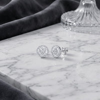 A pair of 10K Gold Baguette Diamond Circle Earrings 5/8 CTW are displayed on a white marble surface, with a glass lid and dark velvet fabric in the background. These exquisite earrings showcase round, diamond-studded studs and baguette diamond accents, adding a touch of sophistication to any look.