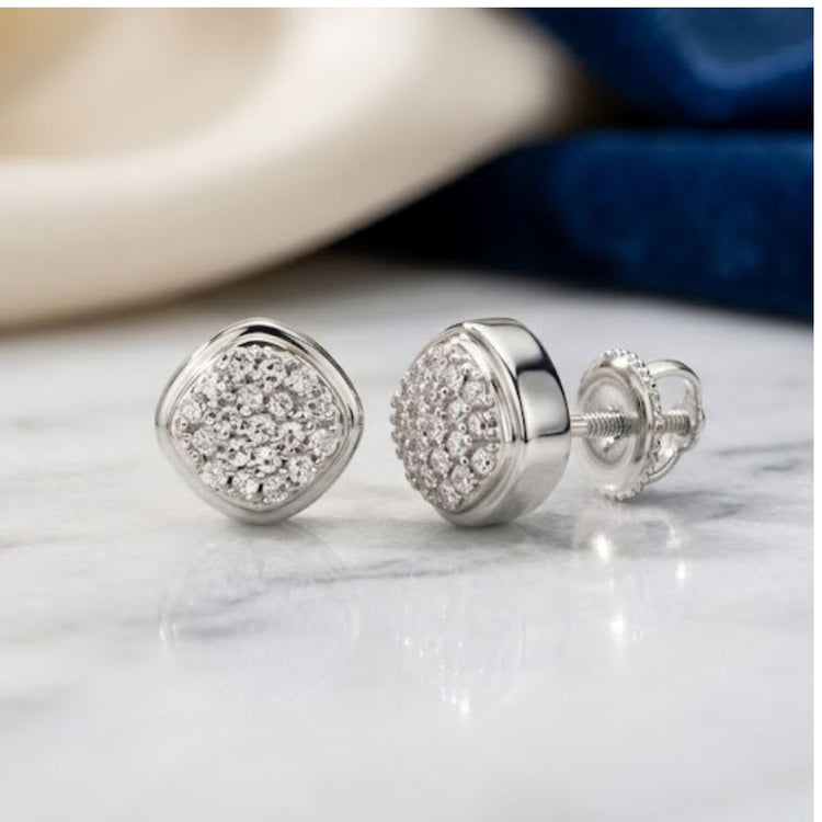 A pair of 1/10 CTW Diamond Cushion Earrings in 10k gold, featuring a cushion-shaped cluster of sparkling natural diamonds, elegantly displayed on a marble surface with a softly blurred background of beige and blue fabric.