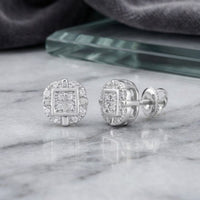 A pair of 10k Gold Diamond Rounded Square Earrings (1/12 Cttw) with a concentric square and round design, set in white metal, displayed on a marble surface.