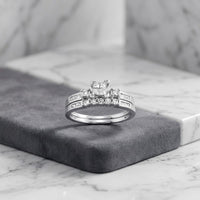 The 10k Gold Princess Diamond Bridal Ring Set 3/8 Cttw is elegantly displayed on a gray velvet surface against a marble background, featuring a radiant white gold engagement ring adorned with multiple sparkling princess-cut diamonds and completed by a matching wedding band for a sophisticated ensemble.