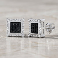 A pair of 10K Gold Black Diamond Square Earrings, totaling 1/4 CTTW, featuring striking black diamonds at the center surrounded by a border of shimmering clear stones and reminiscent of classic diamond jewelry, displayed on a light marble surface.
