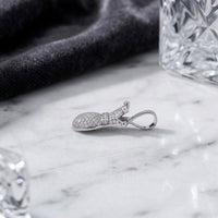 A gleaming 925 Sterling Silver Crown Heart Pendant, encrusted with petite diamonds, rests on a white marble surface beside a dark cloth and clear glass objects. This elegant pendant captures delicate detail and charm, making it an enchanting keepsake.
