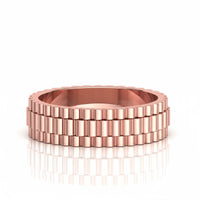 The 14k Gold Men's Link-Inspired Band Ring, featuring a ridged, gear-like design, is stacked with another rose gold ring on a reflective white surface.