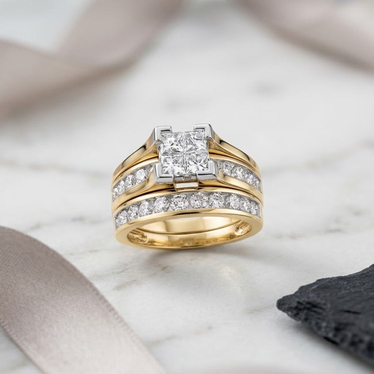 A beautiful 14K Gold Princess Diamond Bridal Ring Set 2 CTTW, showcasing a square-cut centerpiece surrounded by rows of sparkling diamonds, rests on a marble surface beside taupe ribbon and a piece of black stone.