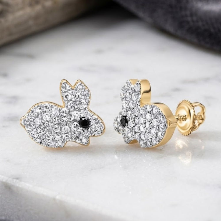 Adorned with sparkling diamonds and striking black diamond eyes, the 10K Gold Black Diamond Earrings 1/4 CTW—whimsically shaped like rabbits—are crafted from gleaming 10K gold and displayed elegantly on a white marble surface.