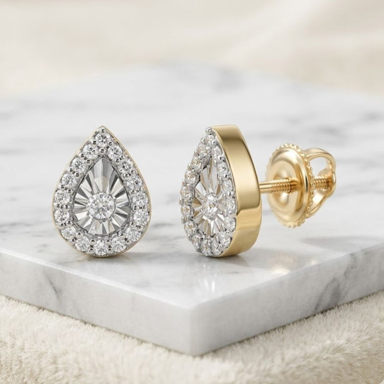 1/10CTW Natural Diamond Pear Earrings in 10K gold, featuring teardrop-shaped diamonds surrounded by smaller stones, are elegantly displayed on a white marble surface.