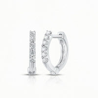 A pair of 10k Gold Round Diamond Hoop Earrings, each featuring a row of sparkling diamonds on the front, is displayed—one shown from the front and one from the side—set against a plain white background.