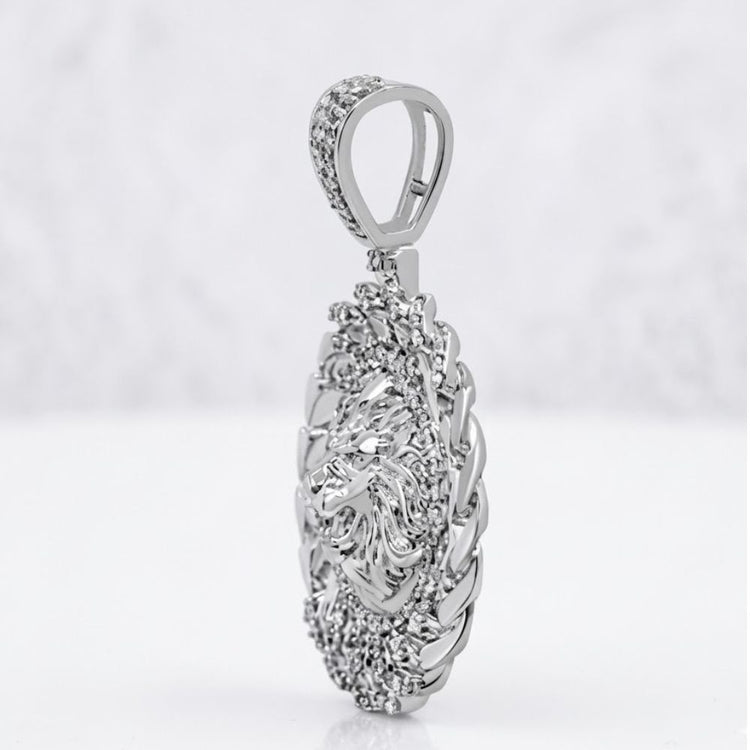 The Diamond Lion Face Cuban Charm 1/2CT Sterling Silver showcases a detailed lion’s head bordered by textured silver, set in an oval design and photographed against a soft, blurred white background.