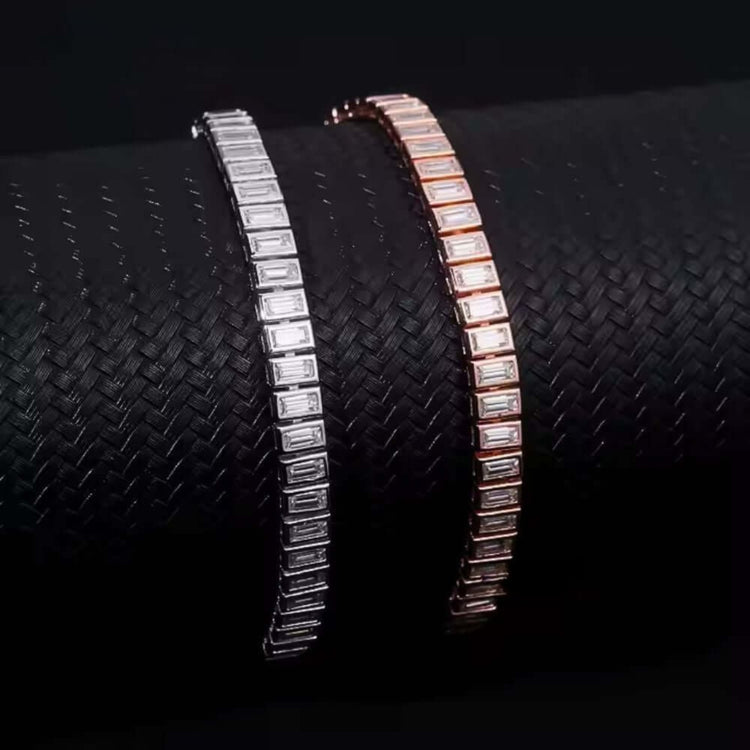 Two Emerald Cut Moissanite Tennis Bracelets—one in 925 sterling silver, one in rose gold—are displayed on a textured black cylindrical surface.