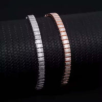 Two Emerald Cut Moissanite Tennis Bracelets—one in 925 sterling silver, one in rose gold—are displayed on a textured black cylindrical surface.
