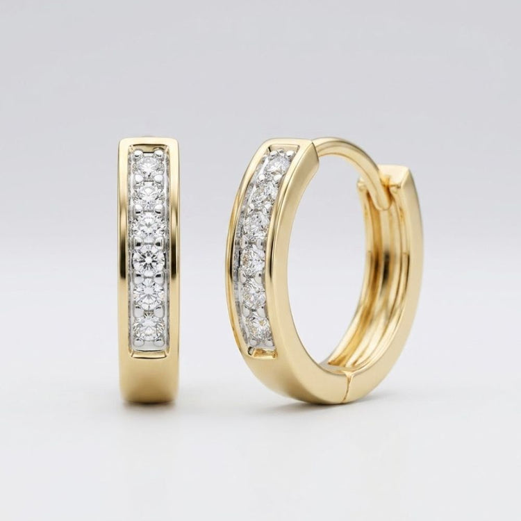 A pair of 1/8CTW round diamond hoop channel earrings in 10K yellow gold, each adorned with a row of sparkling diamonds, displayed against a plain light gray background.