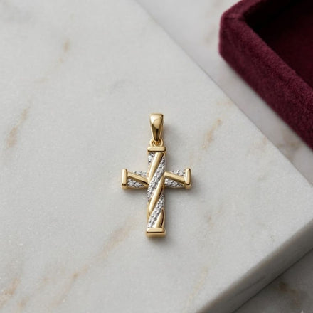A 1/20 CTW Diamond Cross Pendant in 10K gold rests on a white marble surface beside a burgundy jewelry box.