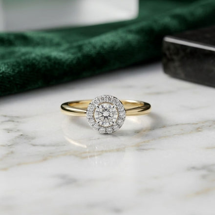 The 14k Gold Round Diamond Halo Engagement Ring, showcased on a marble surface, features a brilliant round diamond center stone encircled by a sparkling halo of smaller diamonds—an elegant and timeless choice for bridal engagement.