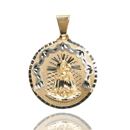 A Circular Caridad Del Cobre, Lady of Charity Pendant in 14k solid yellow gold, features a raised religious figure with a child, detailed rays in the background, and an ornate border, displayed on a white reflective surface.