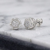 A pair of 1/4CTW Natural Diamond Gift Earrings in sterling silver rests on a white marble surface.