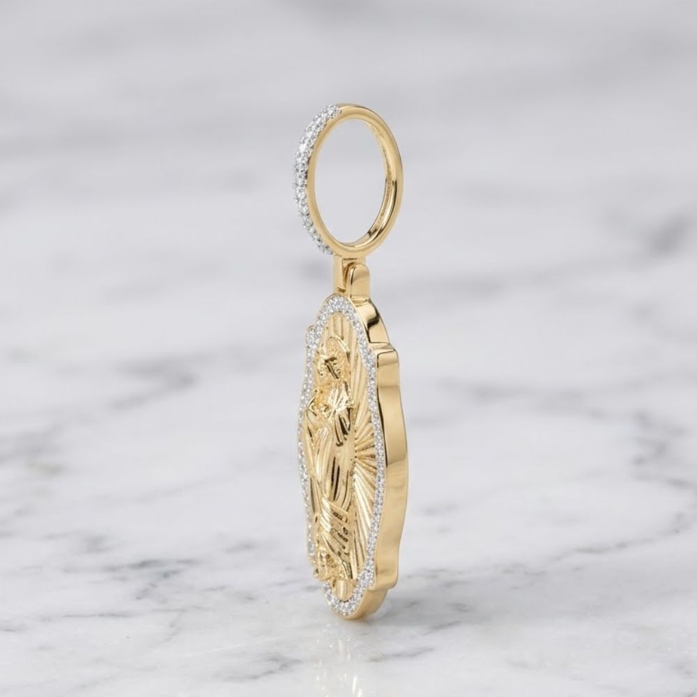 The Diamond Virgin Prayer Charm 3/8CT in 10K gold features an engraved religious figure with sparkling white stones on the border and loop, displayed upright on white marble—a bold pendant for men.