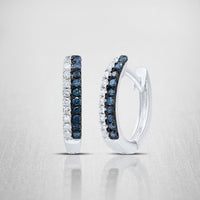 A pair of 10K Blue Diamond Huggie Earrings (1/5 CTTW Gold) featuring two rows—one of dark blue diamonds and one of clear stones—set on a light, textured background.