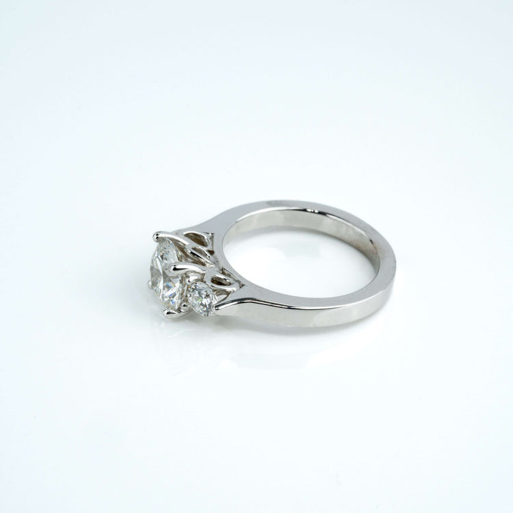 The 3.08CTW Round Trilogy Lab Diamond Engagement Ring in 14K white gold features a large central lab diamond with two smaller side stones on a simple band, shown against a white background.
