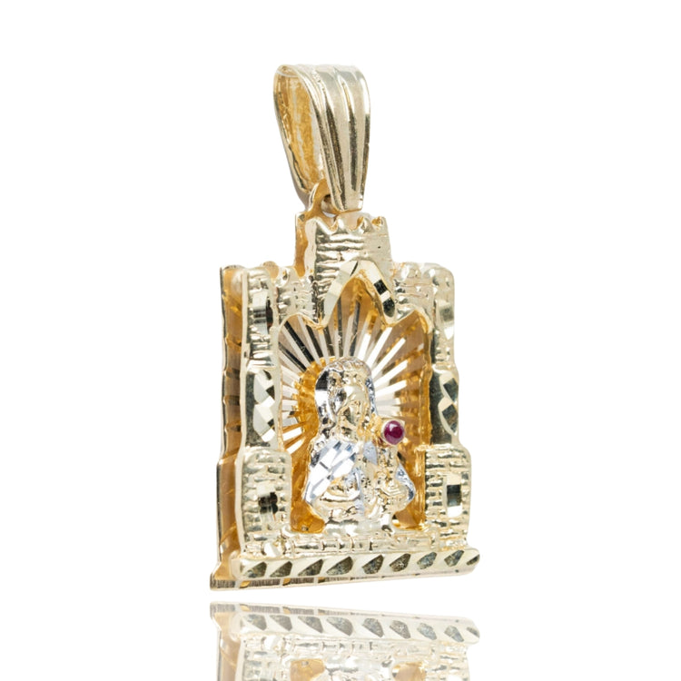 The St. Barbara Castle Shaped Pendant in 10k gold features a religious figure with halo, engraved patterns, a red gemstone accent, and a polished, reflective finish. This men's jewelry piece has a textured, castle-shaped design.