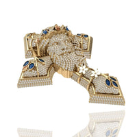 A Diamond Jesus Head Pendant with sapphire and ruby accents, featuring blue gemstones, white flower motifs, and intricate detailing, set against a white background with a subtle reflection below.