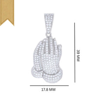 The 925 Silver Moissanite Praying Hands Charm is a pendant shaped like praying hands, set with white stones and topped with a gold ribbon. It measures 39mm tall by 17.8mm wide.
