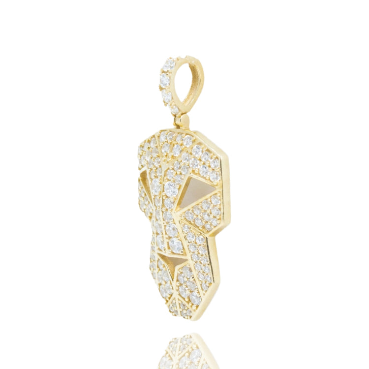 The Edge Mask Pendant in 10k solid gold is a bold men’s accessory featuring a stylized face with numerous small cubic zirconia stones, shown at an angle on a white background with its reflection visible below.
