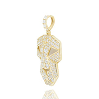 The Edge Mask Pendant in 10k solid gold is a bold men’s accessory featuring a stylized face with numerous small diamonds, shown at an angle on a white background with its reflection visible below.