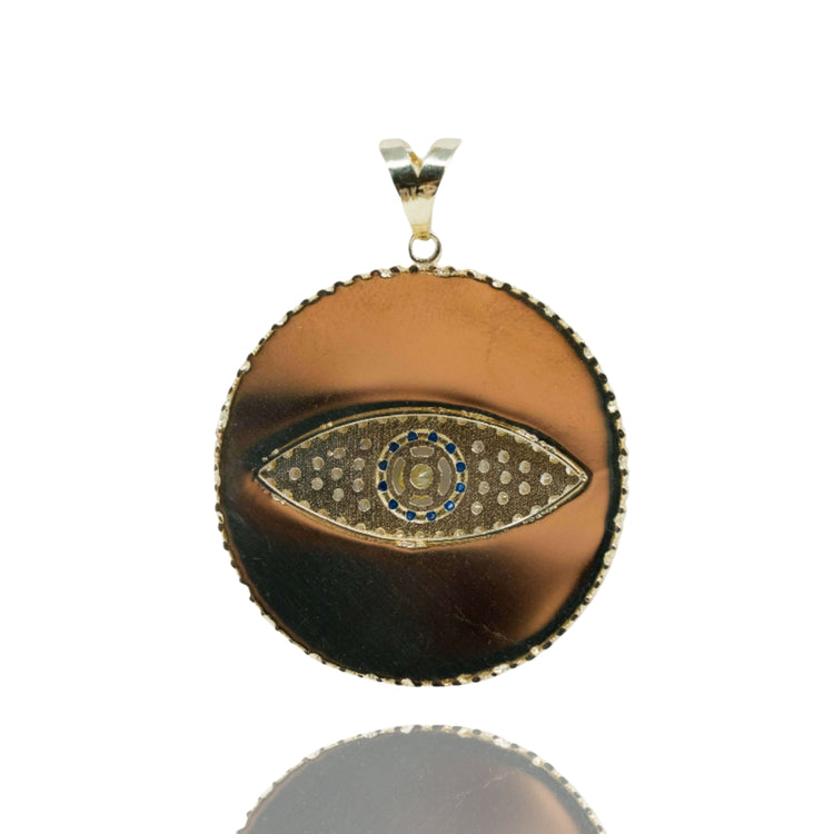 The Eye Pendant – 10k is a round gold pendant with a polished metallic finish, showcasing a central eye design accented with blue, gold, and silver details—an elegant choice for men's jewelry.