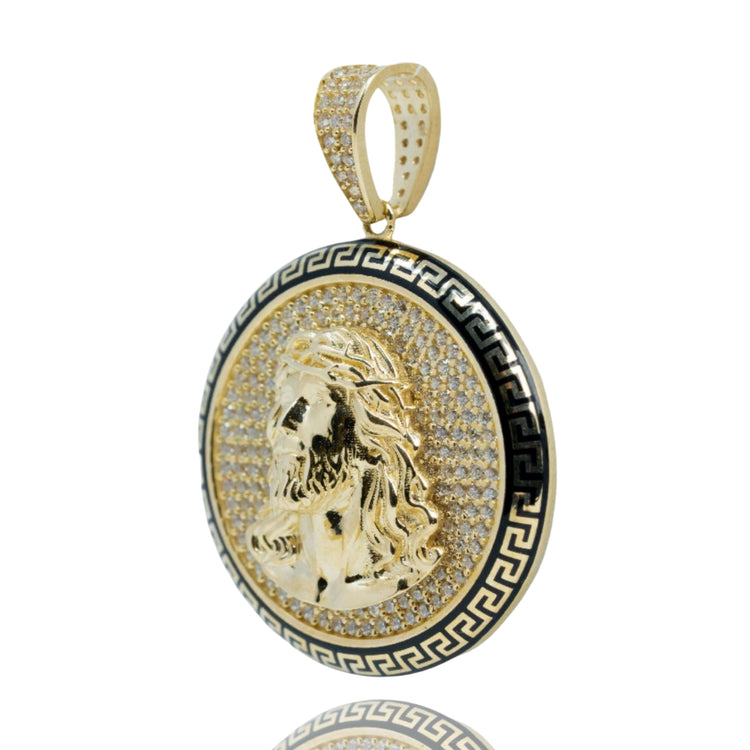 The Christ Circular Portrait Pendant in 10k gold features a raised Jesus profile with cubic zirconia accents, framed by a black and gold Greek key border—a striking piece of religious jewelry shown on a reflective white background.