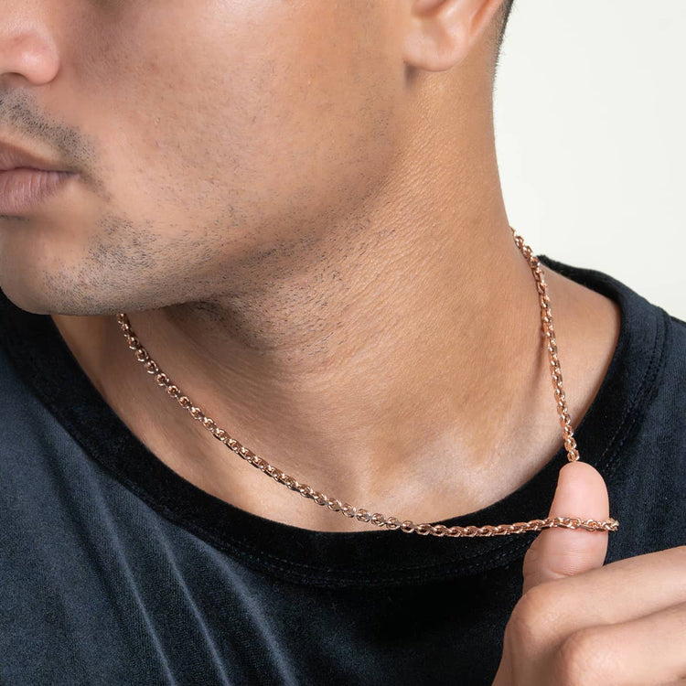 A person in a black shirt and gold chain necklace holds part of the 3.5mm Solid Rose Gold Cable Link Chain between their fingers, its links gleaming as their jawline and mouth are partially visible.