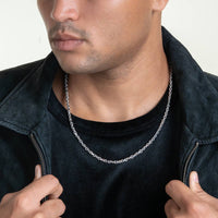 A man wearing a black shirt and dark jacket holds his jacket collar open, showcasing a 3.5mm Solid White Gold Power-Cable Link Chain around his neck against a plain light background.