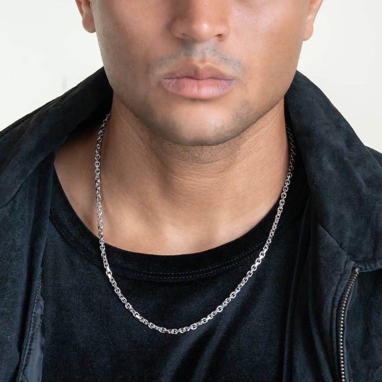 A person in a black shirt and jacket is shown from the shoulders up, wearing the 3.5mm Solid White Gold Power-Cable Link Chain necklace against a plain, light background.