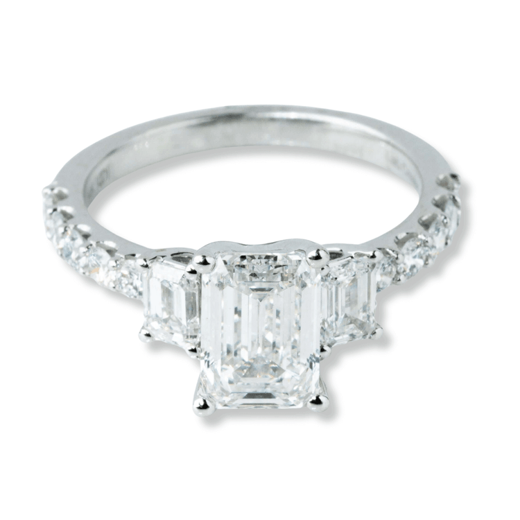 The 3.8 CTW 14k White Gold Three Stone Emerald Engagement Ring features a large emerald-cut diamond, two smaller rectangular lab-grown diamonds, and a band set with sparkling round diamonds.
