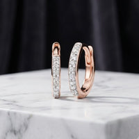 A pair of 1/10ctw natural diamond hoop earrings in 10K gold displayed on a white marble surface with a dark, blurred background.