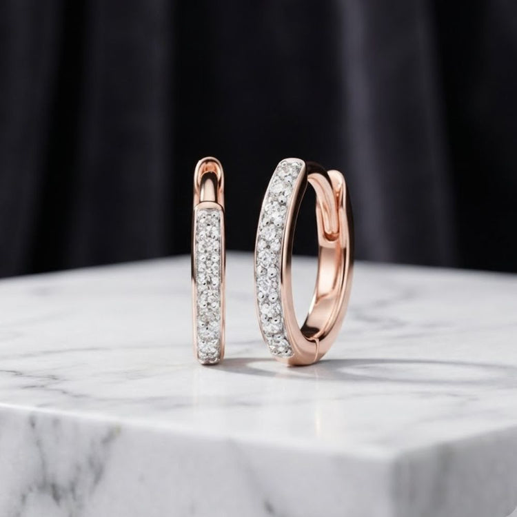 A pair of 1/10ctw natural diamond hoop earrings in 10K gold displayed on a white marble surface with a dark, blurred background.