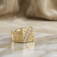 10k Yellow Gold Round Diamond Nugget Fashion Ring 1/2 Cttw featuring a textured, geometric nugget pattern and a diagonal row of sparkling round diamonds, displayed on a marble surface with a soft beige fabric background—an elegant ring that embodies both modern flair and timeless sophistication.
